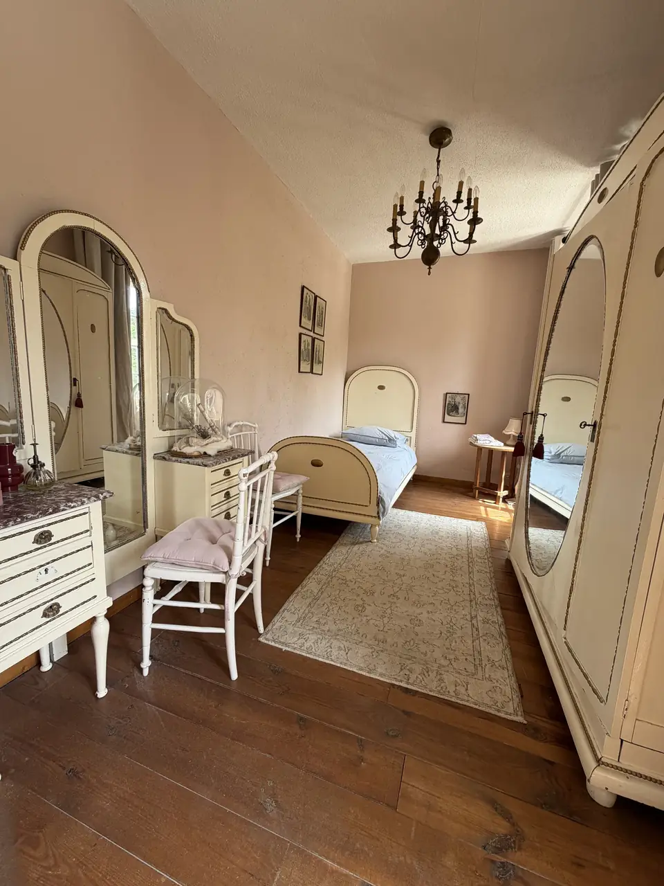 Een kamer met een crèmekleurig eenpersoonsbed, een spiegelkast en een kaptafel.