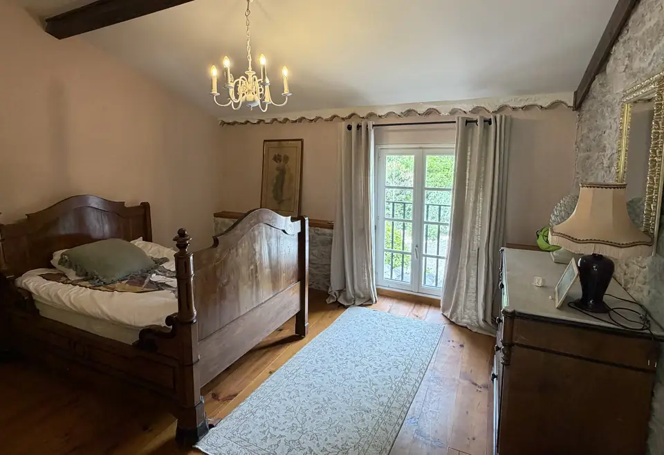 Een slaapkamer met roze muren, een donker houten bed, een kroonluchter en openslaande deuren.