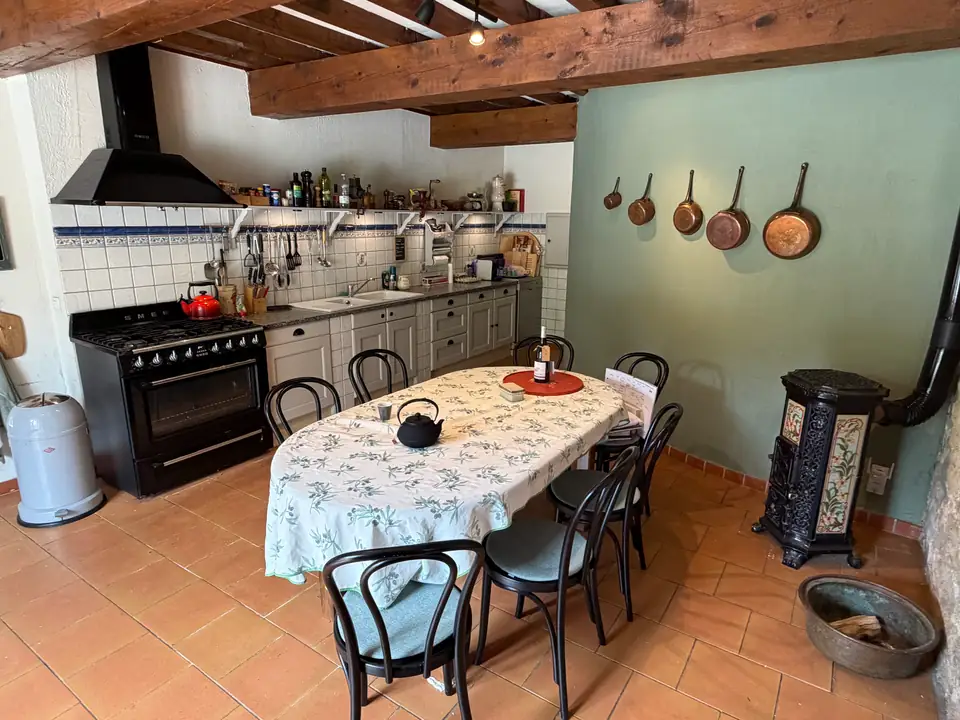 De keuken: koperen pannen aan de groene muur, een zwart fornuis, blauw-witte tegels en een ovale tafel.